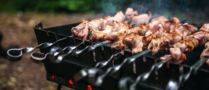 Barbecue with delicious grilled meat on skewer on brazier outside at summertime. Preparing pork steaks with smoke during picnic at the nature. Closeup view at hot BBQ