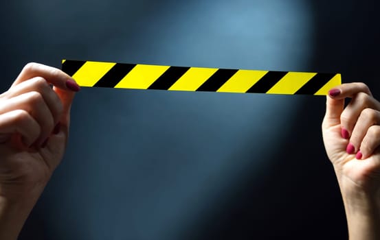 Hands holding yellow tape with black and yellow stripes on a dark background . Warning ribbon.