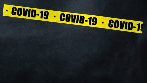 Yellow tape with text COVID-19 on a dark background. Warning ribbon.