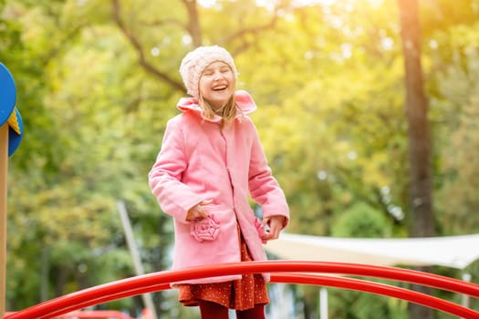 Pretty girl kid playing on playground at autumn day outdoors and laughing. Female child having fun nd smiling at the street