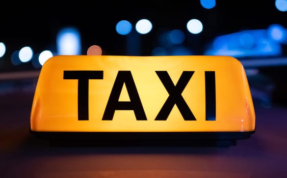 Taxi car yellow light sign on dark street at night with illumination. Cab service symbol with neon glowing