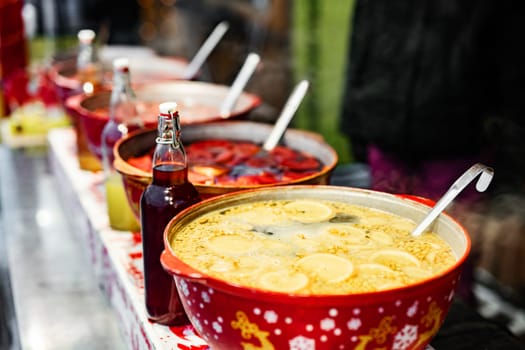 Beverages fruits and berries hot mulled wine in red pots in street food market. Colorful hot drinks at fair festival outdoors closeup