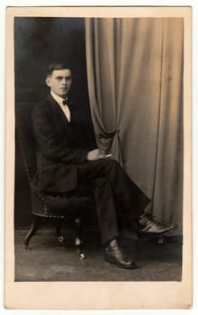 PRAGUE, THE CZECHOSLOVAK REPUBLIC - CIRCA 1920s: Vintage photo shows young man sits on armchair. Antique black & white studio portrait.