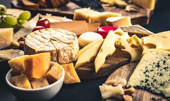 Different kinds of cheese on wodden plate table served with grape and tomato. Organic parmesan, brie and camambert set delicatessen collection