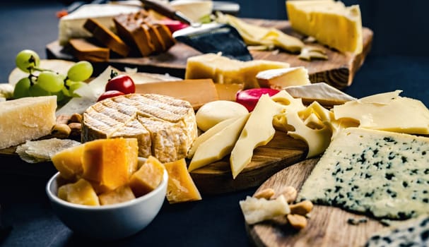 Different kinds of cheese on wodden plate table served with grape and tomato. Organic parmesan, brie and camambert set delicatessen collection