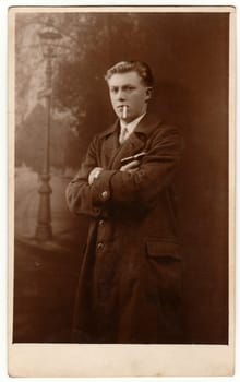 LIBEREC (REICHENBERG), THE CZECHOSLOVAK REPUBLIC - CIRCA 1920s: Vintage photo shows young man poses with cigarette outdoors. Antique black white portrait.