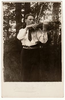 THE CZECHOSLOVAK REPUBLIC - MARCH 8, 1923: Vintage photo shows young man plays the violin outdoors. Antique black & white photo.
