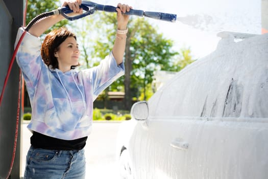 Girl washing a car in a self-service car wash station with wahing foam. Wash car self-service station.