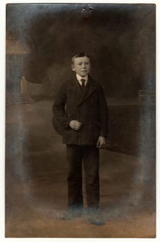 THE CZECHOSLOVAK REPUBLIC - CIRCA 1920s: Vintage photo shows boy wears suit and tie. Antique black white photo taken outdoors. On top of the image is imprint of drawing pin. Photo has dark tint.