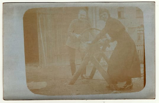 GERMANY - CIRCA 1920s: Vintage photo shows man and woman cutting a log. They work in the back yard. Photo has error obtained during photo process. Antique black white photo.