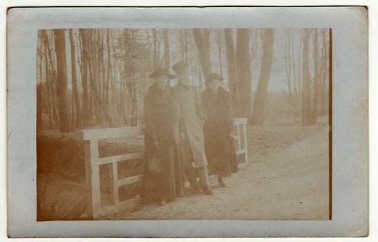 GERMANY - CIRCA 1920s: Vintage photo shows women and soldier during a walk. They stand on the bridge. Photo has error obtained during photo process. Antique black white photo.