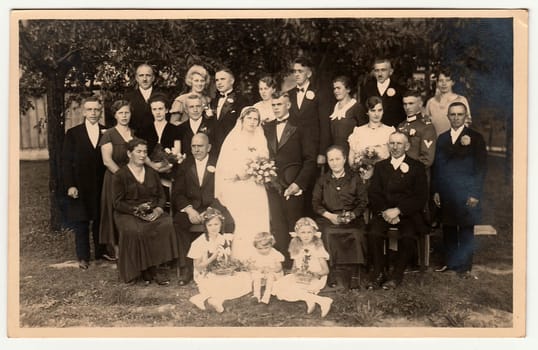 THE CZECHOSLOVAK REPUBLIC - CIRCA 1920s: Vintage photo shows newlyweds with wedding guests. Photo was taken in the summer garden. Black white photo.
