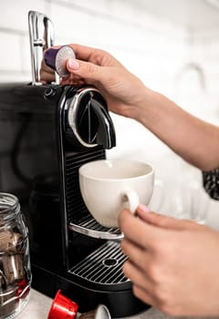Girl hand put capsule to coffee machine at home closeup. Woman preparing italian caffeine beverage using professional espresso maker