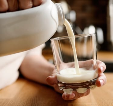 Girl pouring milk to glass for breakfast. Woman with white organic latte.
