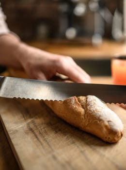 Girl hand cut french baguette with knife at kitchen. Tasty rustic fresh bread from for breakfast meal