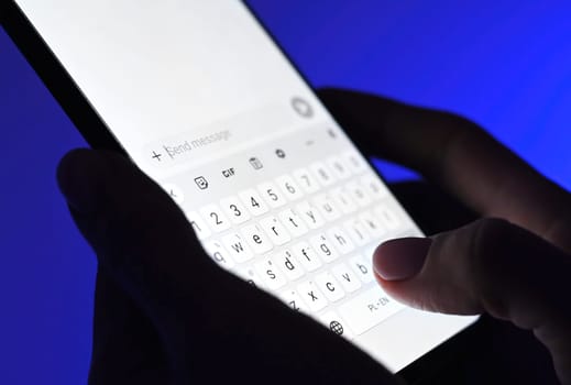 Girl typing message on a smartphone against blue background. Close up viwe of white sceen.