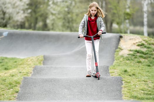 Beautiful little girl rides a scooter in a extreme ride park