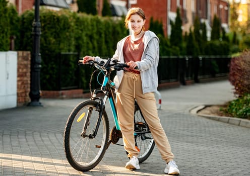 Cute laughing girl standing with a bike in the evening in a calm city.