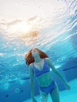 Teen girl swimming under water in blue pool. Pretty female teenager diving and enjoying summer activity
