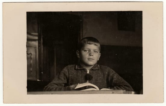 EILENBURG, GERMANY - CIRCA 1950s: Vintage photo shows pupil boy with book at the desk. Black & white retro photo.