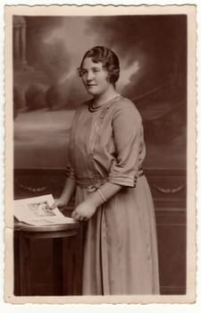 EILENBURG, GERMANY - CIRCA 1920s: Vintage photo shows mature woman poses with book in a photography studio. Antique black & white studio portrait.