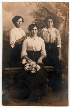 NARSDORF, GERMANY - NOVEMBER 9, 1912: Vintage photo shows three women pose in a photography studio. Black white antique studio portrait.