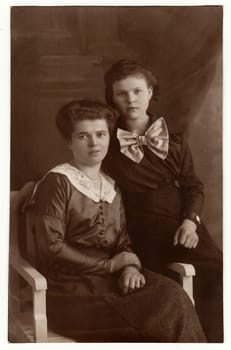 BERLIN, GERMANY - 1919: Vintage photo shows mature woman and her daughter pose in a photography studio. Black white antique studio portrait.