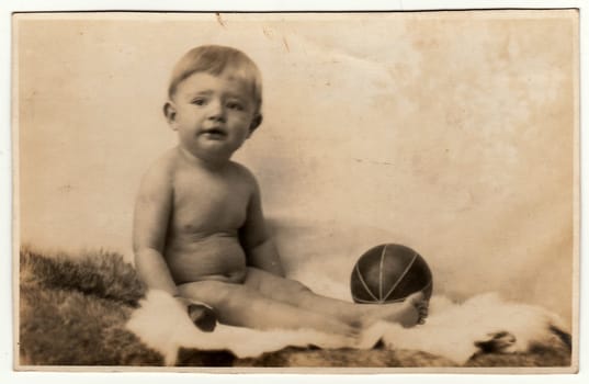 FRYDLANT, THE CZECHOSLOVAK REPUBLIC- CIRCA 1940S: Vintage photo shows toddler boy with balls sits on a fur. Black white antique studio portrait.