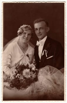 LIBEREC (REICHENBERG), THE CZECHOSLOVAK REPUBLIC - CIRCA 1940s: Vintage photo of newlyweds with wedding bouquet. Bride wears wedding veil headdress. Groom wears posh clothing, white bow-tie. Black white antique studio portrait.