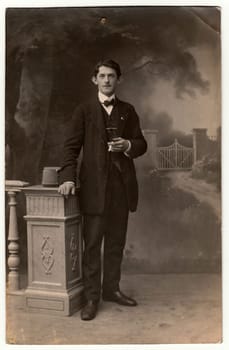 AUSTRIA-HUNGARY - CIRCA 1910s: Vintage photo shows man with cigarette poses in a photography studio. Photo with dark sepia tint. Black white studio portrait.