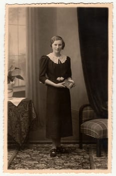 THE CZECHOSLOVAK REPUBLIC - CIRCA 1930s: Vintage photo shows an elegant woman with book poses in a photography studio. Photo with dark sepia tint. Black white studio portrait.