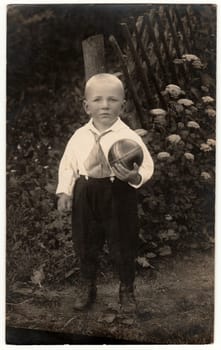 THE CZECHOSLOVAK REPUBLIC - CIRCA 1930s: Vintage photo shows a small boy with ball poses outdoors. Black white antique photo.