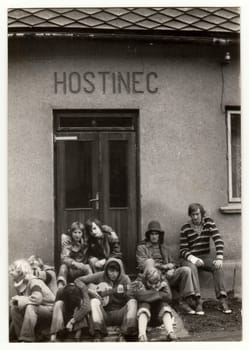 THE CZECHOSLOVAK SOCIALIST REPUBLIC - CIRCA 1980s: Vintage photo shows young hikers in front of the pub. One of them plays the guitar. Antique black white photo.