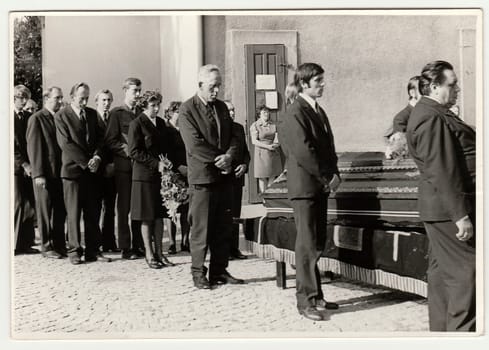 THE CZECHOSLOVAK SOCIALIST REPUBLIC - CIRCA 1980s: Vintage photo shows people during funeral. The coffin lies on bier next to church. Black white antique photo.