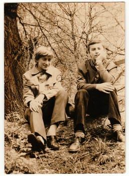 THE CZECHOSLOVAK SOCIALIST REPUBLIC - CIRCA 1980s: Vintage photo shows boys sit on the grass outdoors. Antique black white photo.