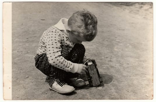 THE CZECHOSLOVAK SOCIALIST REPUBLIC - CIRCA 1960s: Vintage photo shows boy plays with toy car outdoors. Antique black & white photography.