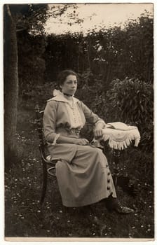 THE CZECHOSLOVAK REPUBLIC - CIRCA 1930s: Vintage photo shows woman sits on a historic chair at the tiny table in the garden. Black white antique photography.