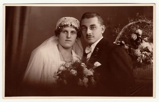 CHRASTAVA (KRATZAU), THE CZECHOSLOVAK REPUBLIC - CIRCA 1930s: Vintage photo of newlyweds. Bride wears a veil and holds wedding bouquet. Black & white antique studio portrait.