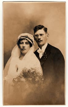 THE CZECHOSLOVAK REPUBLIC - CIRCA 1930s: Vintage photo of newlyweds. Bride wears a veil and holds wedding bouquet. Groom wears black suit and white bow tie. Black white antique studio portrait