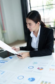 Portrait of a thoughtful Asian businesswoman looking at financial statements and making marketing documents plans on her desk.