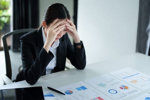 A portrait of a beautiful Asian female employee showing a stressed face while using financial documents on her desk.