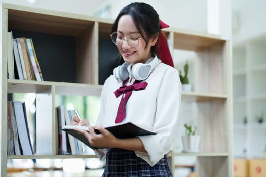 Portrait of a beautiful young Asian student using a notebook to take notes in the library.