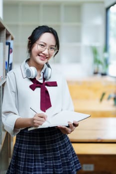 Portrait of a beautiful young Asian student using a notebook to take notes in the library.