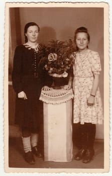 GERMANY - CIRCA 1930s: Vintage photo shows women pose in photo studio with bouquet on a white pedestal. Black white antique photography.