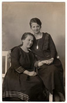 GERMANY - CIRCA 1930s: Vintage photo shows women pose in photo studio. They sit on white historic bench. Black white antique photography.