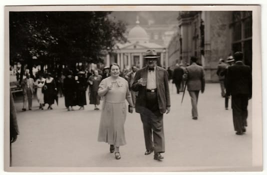 MARIANSKE LAZNE, THE CZECHOSLOVAK REPUBLIC - JUNE, 1936: Vintage photo shows a mature couple goes for a walk in the spa resort. Black white antique photography.