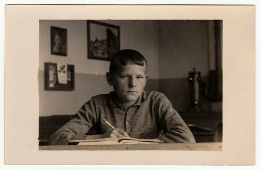 EILENBURG, GERMANY - CIRCA 1940s: Vintage photo shows young boy (pupil, student) sits at the classroom. Black white antique photography.