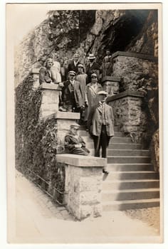 THE CZECHOSLOVAK REPUBLIC - CIRCA 1940s: Vintage photo shows people stand on the stairs outdoors. Some of them wears leather helmet for driving of car. Black white antique photography.