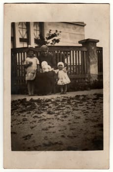 MALENICE (VOLARY),THE CZECHOSLOVAK REPUBLIC - CIRCA 1920s: Vintage photo shows woman and children pose in front of house. The woman holds teddy bear. Black white antique photo.