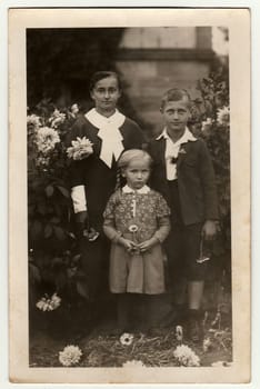 GERMANY - CIRCA 1940s: Vintage photo shows young woman with children (boy and girl) pose in the garden. Black white antique photography.